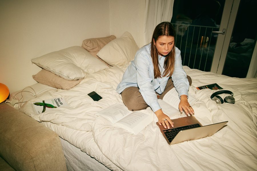 Studerende med laptop og bøger på sengen