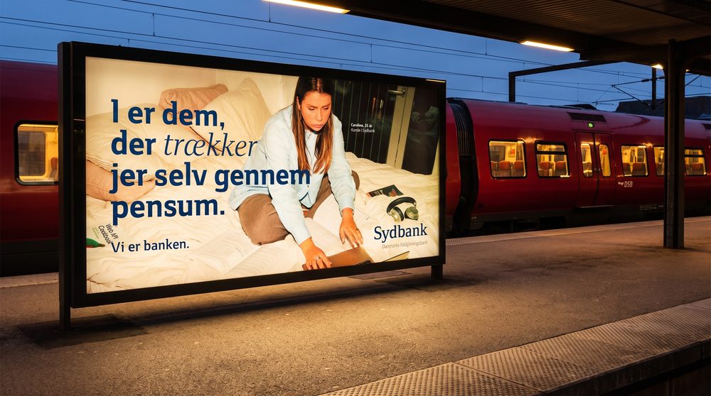 Sydbank-railboard der gløder i skumringen på dansk perron